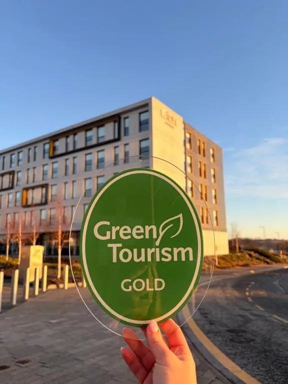 a person holding a green tourism gold sign in front of a building at Aloft Aberdeen TECA in Aberdeen