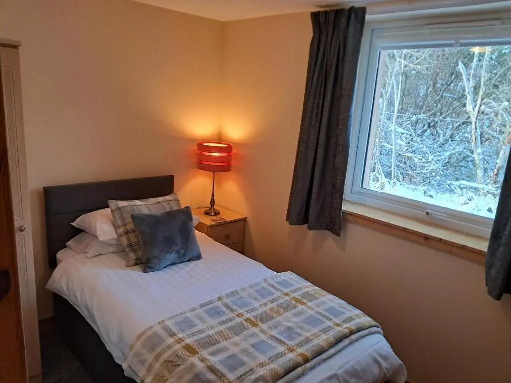 a bedroom with a bed with a window and a lamp at Roe Deer Cottage in Beauly