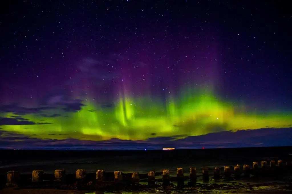 an aurora in the sky over the ocean at night at Cliffside in Lossiemouth