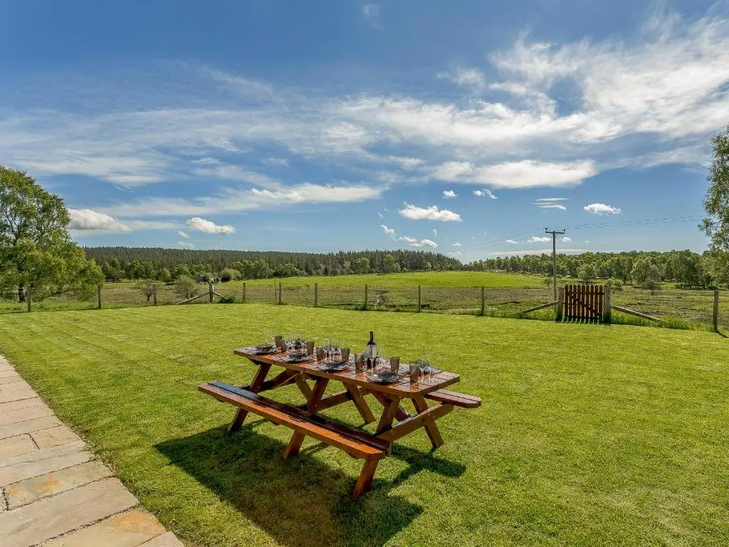 a picnic table in a field with a view of a farm at Sunnyside House in Duthil