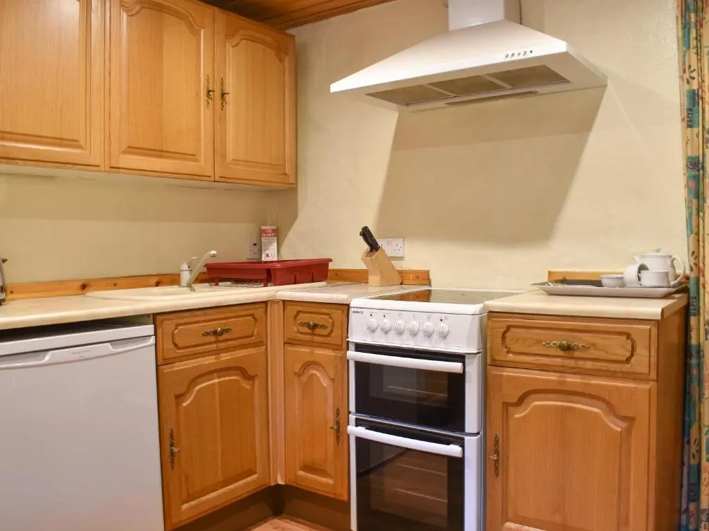 a kitchen with wooden cabinets and a white stove top oven at Burnmouth in Balnaboth