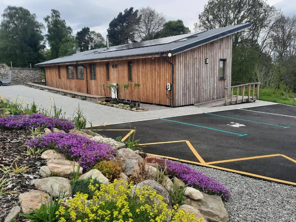 a building with a parking lot with purple flowers at Carnmore Cottage in Inverness