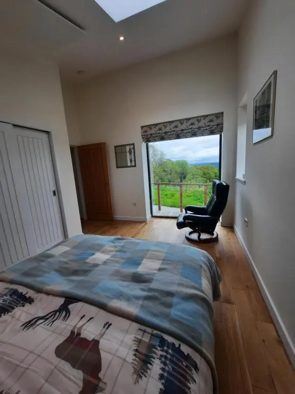 a bedroom with a bed and a chair and a window at Carnmore Cottage in Inverness