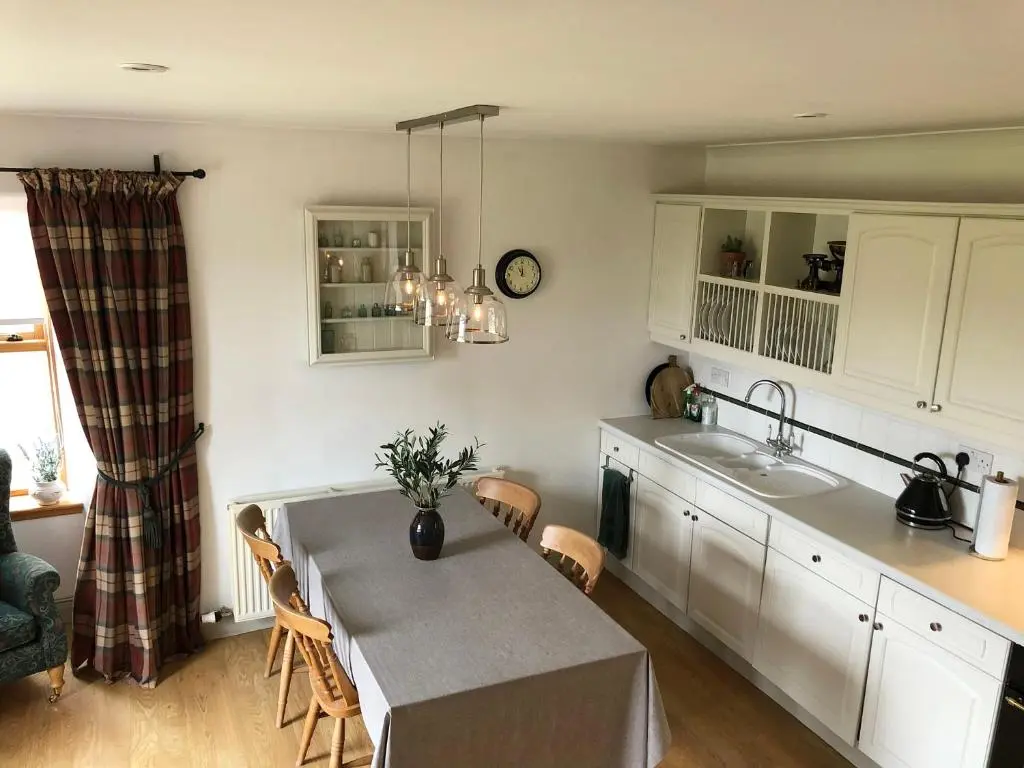 a kitchen with white cabinets and a table and a sink at Glenmuir Cottage in Dornoch