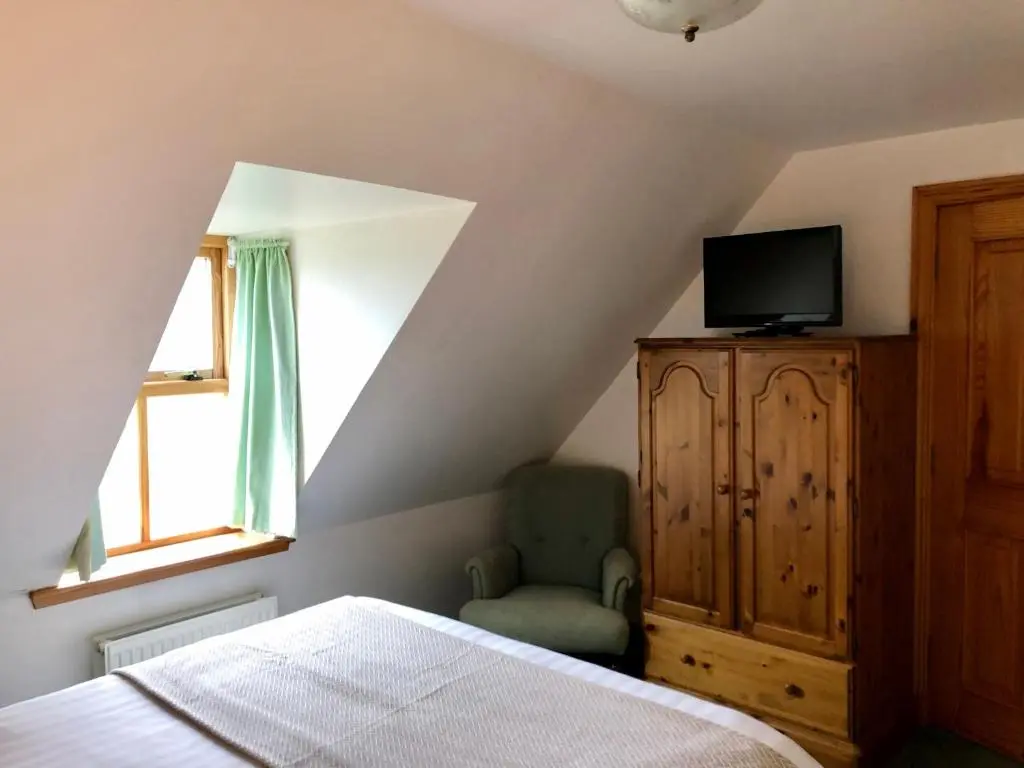a bedroom with a bed and a tv and a chair at Glenmuir Cottage in Dornoch