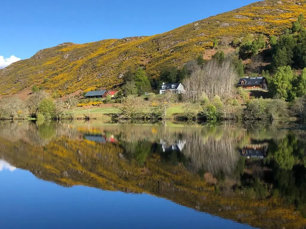 a house on a hill next to a lake at Nan's Cottage in Beauly