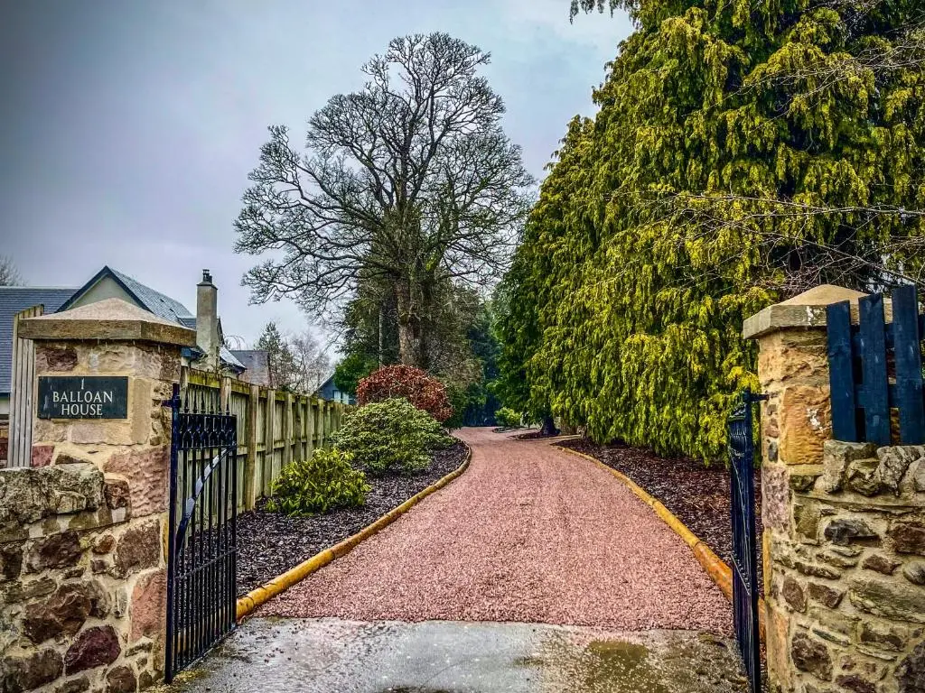 a driveway of a house with a fence and trees at Balloan Cottage Cowshed in Inverness