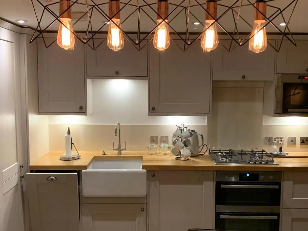 a kitchen with white cabinets and a sink and lights at Balloan Cottage Cowshed in Inverness