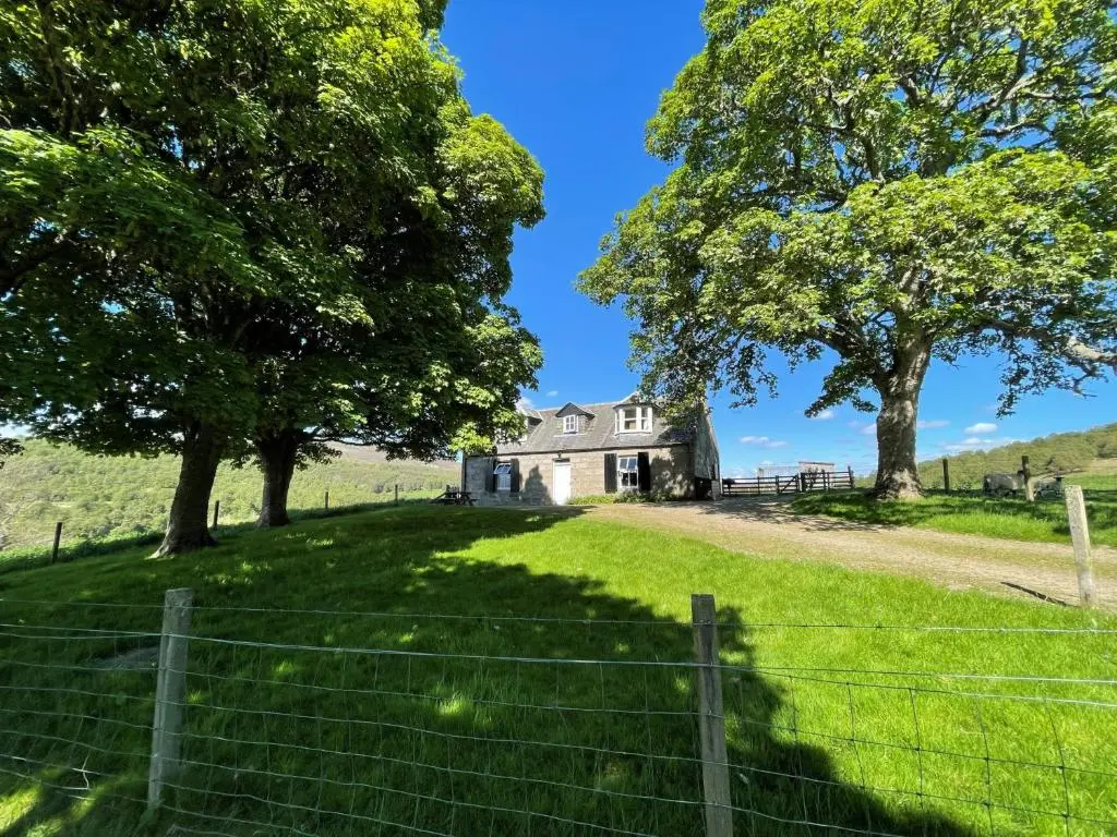 an old house on a hill with trees and a fence at West Gorton in Grantown on Spey
