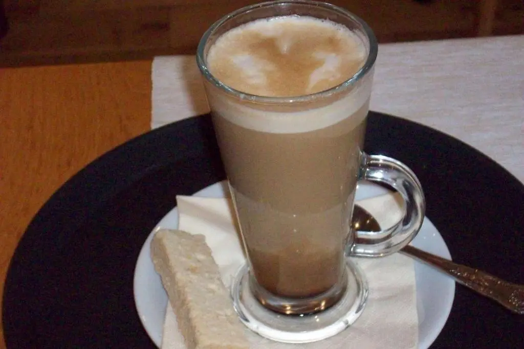 a glass of coffee on a plate with a piece of bread at Lairg Highland Hotel in Lairg