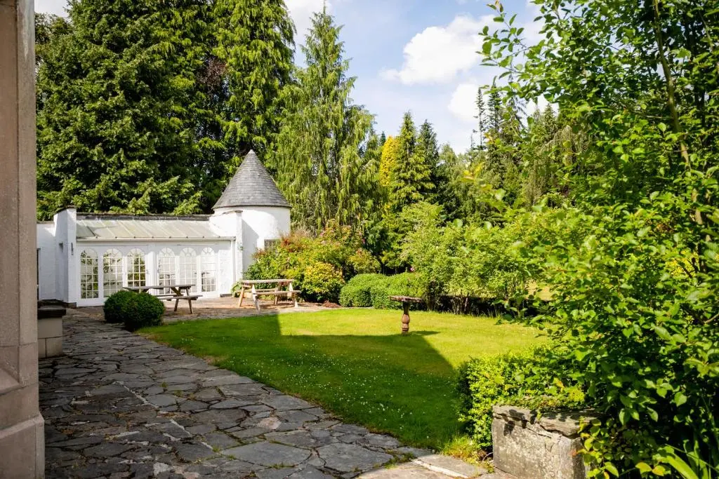 a garden with a white greenhouse in the background at Scatwell House in Garve