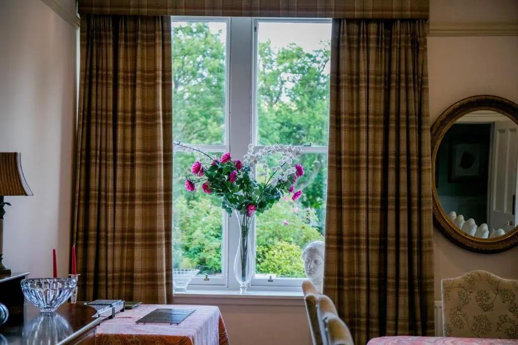 a vase of flowers sitting in a window with a table at Scatwell House in Garve