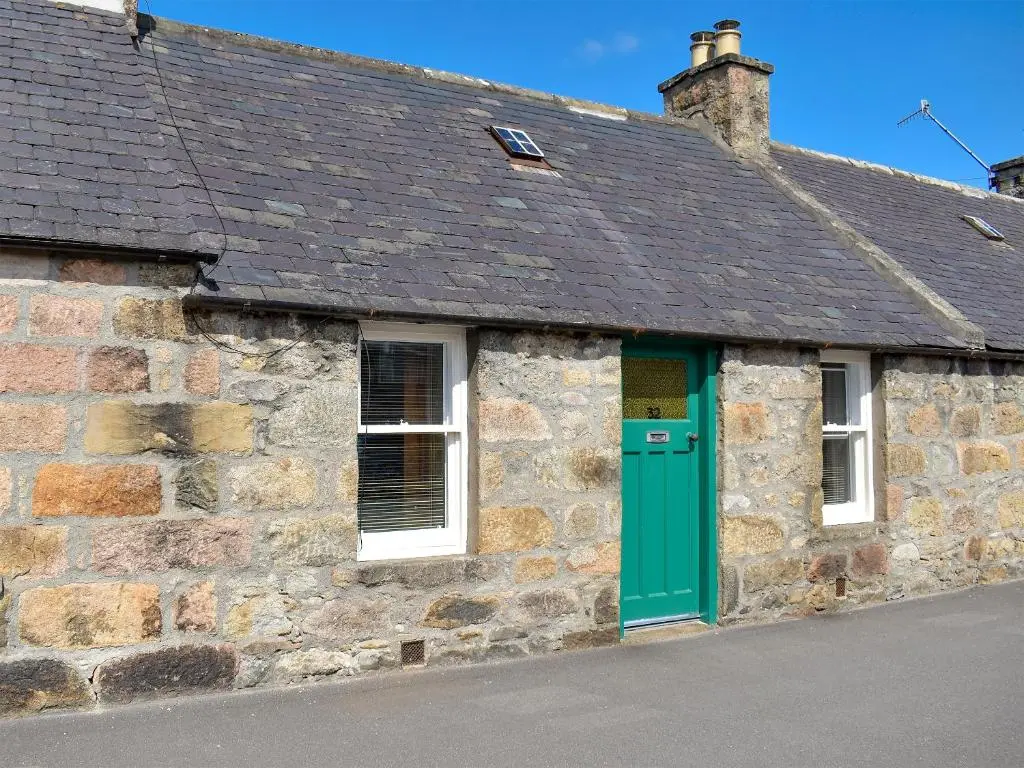 an old stone building with a green door at Spey Cottage in Aberlour