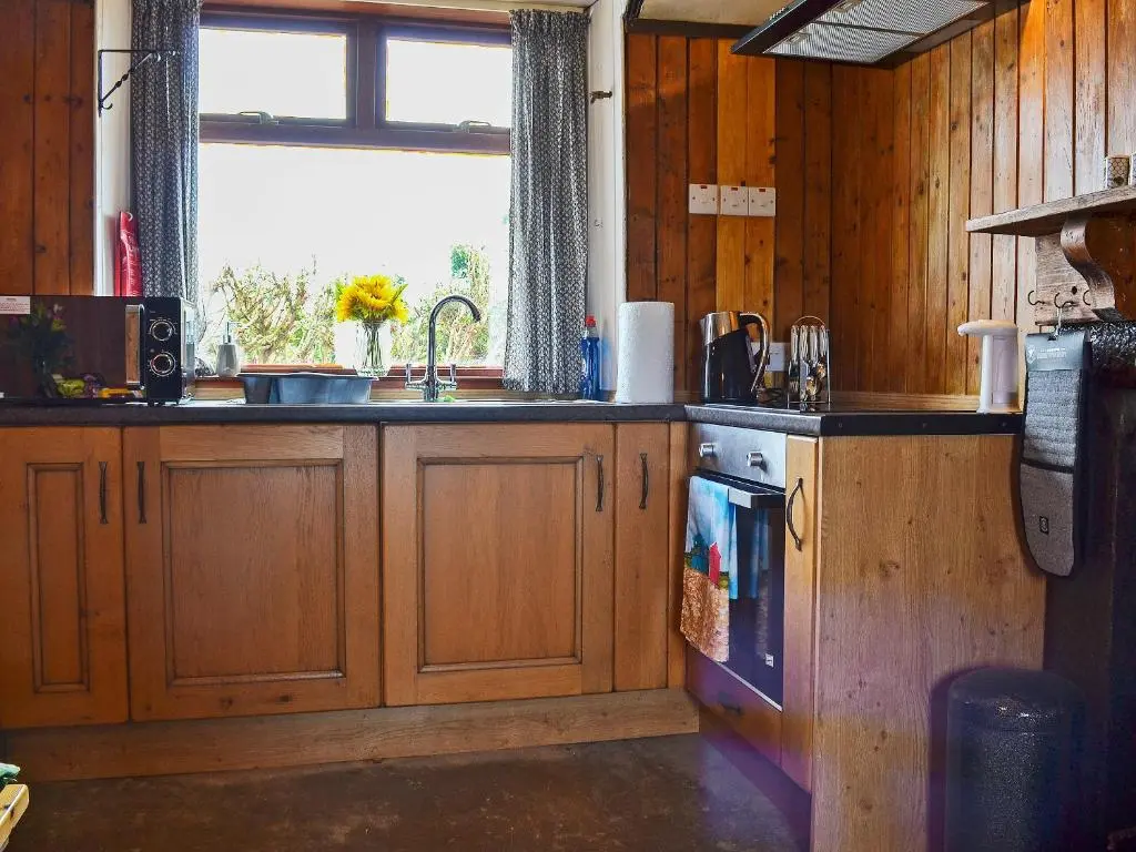 a kitchen with wooden cabinets and a sink and a window at Mains Of Auchmedden Cottage in Pennan