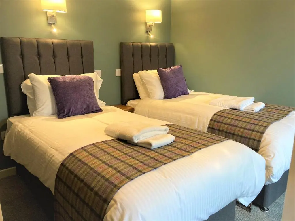 two beds in a hotel room with towels on them at The 1645 Inn in Nairn