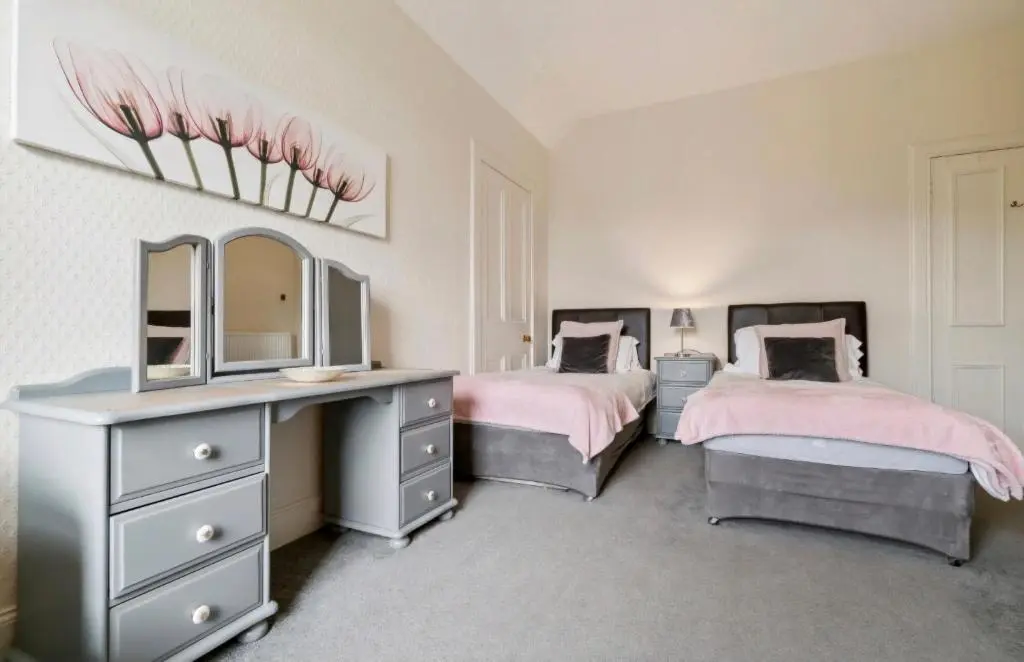a bedroom with two beds and a dresser and a mirror at Kinnaird Country House with Hot Tub in Pitlochry