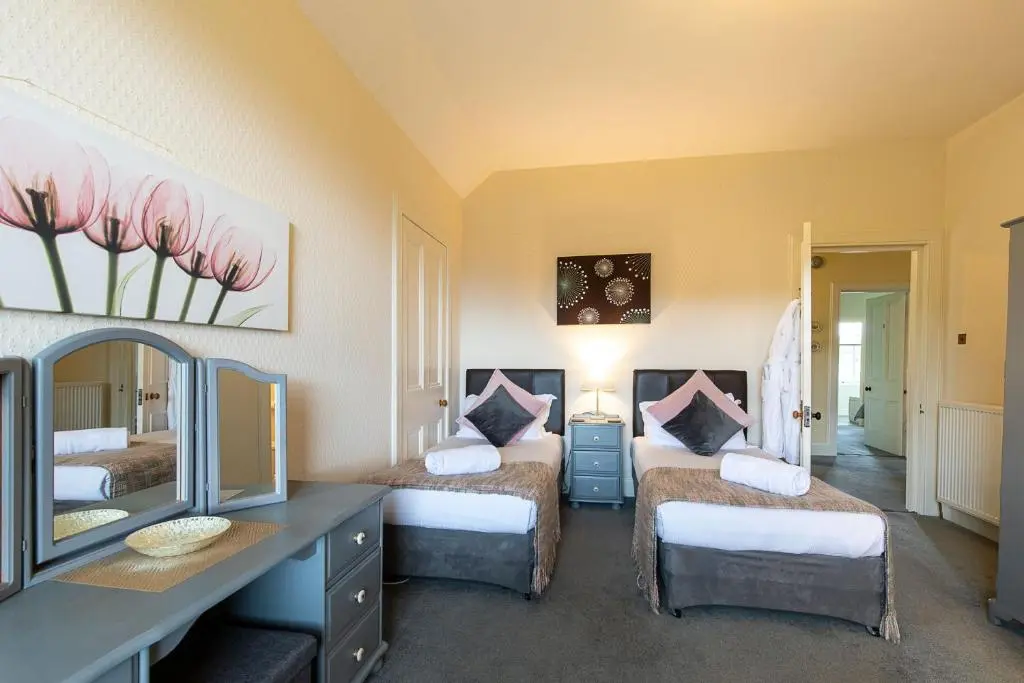 a bedroom with two beds and a desk with a mirror at Kinnaird Country House with Hot Tub in Pitlochry