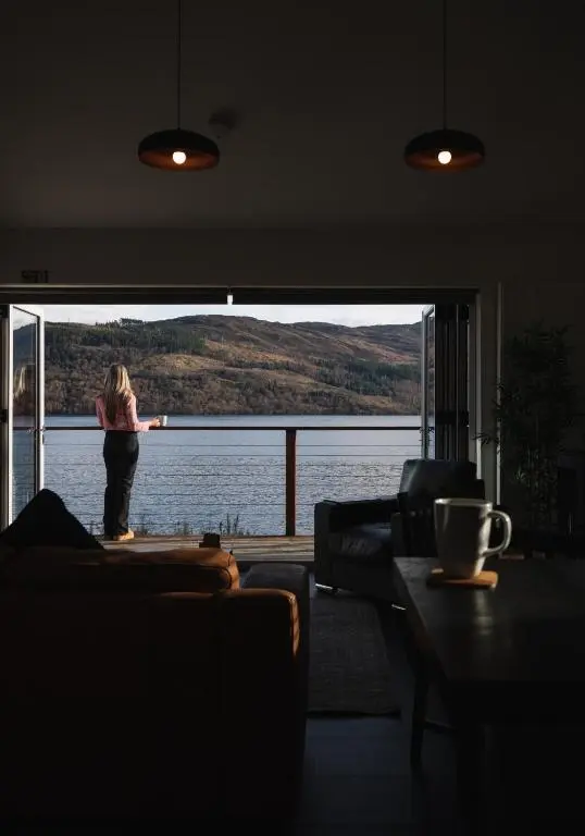 a woman standing in a living room looking out at the water at Shoreland Lodges - Holly Lodge in Fort Augustus
