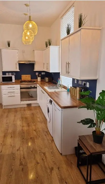 a kitchen with white cabinets and a wooden floor at City Centre Flat, Harbour View in Inverness