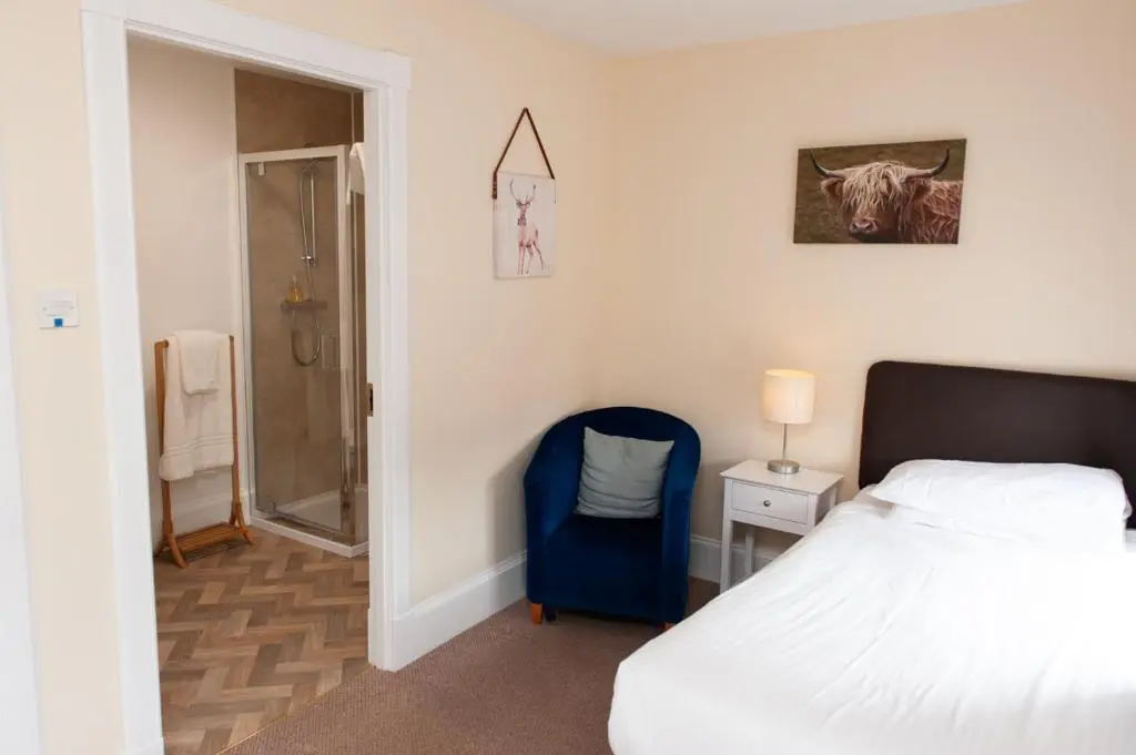 a bedroom with a bed and a blue chair at Alban and Abbey House in Inverness