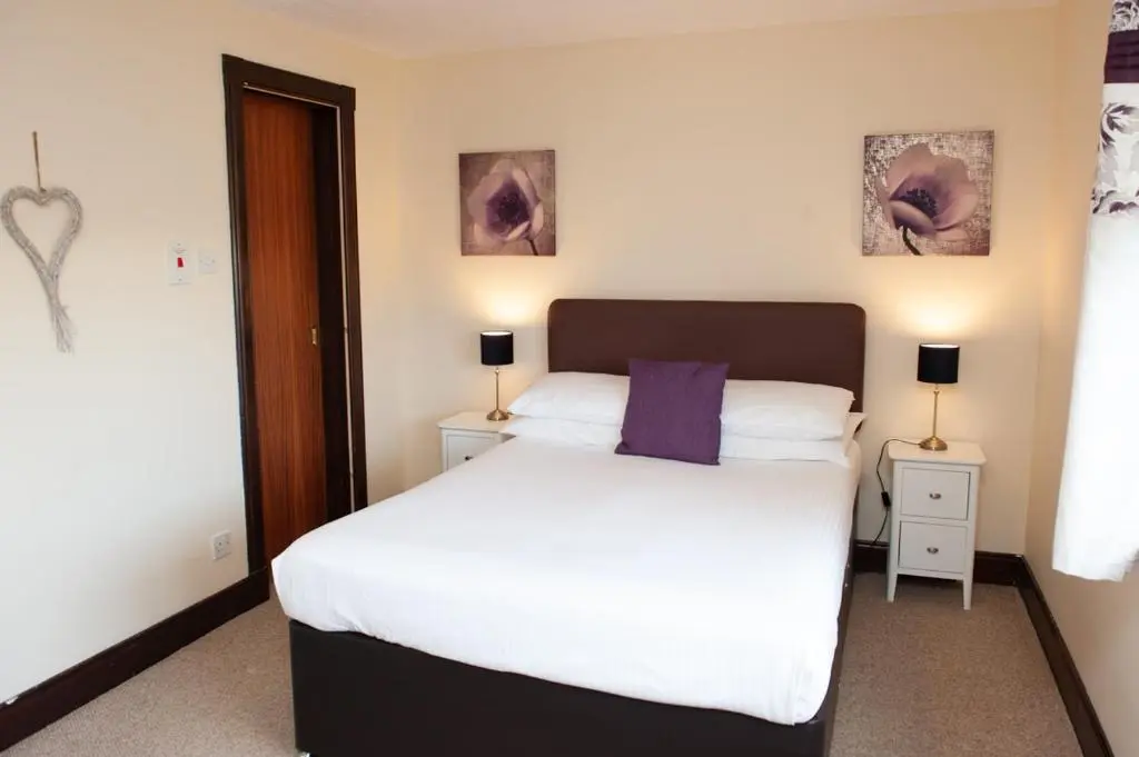 a bedroom with a white bed with a purple pillow at Alban and Abbey House in Inverness