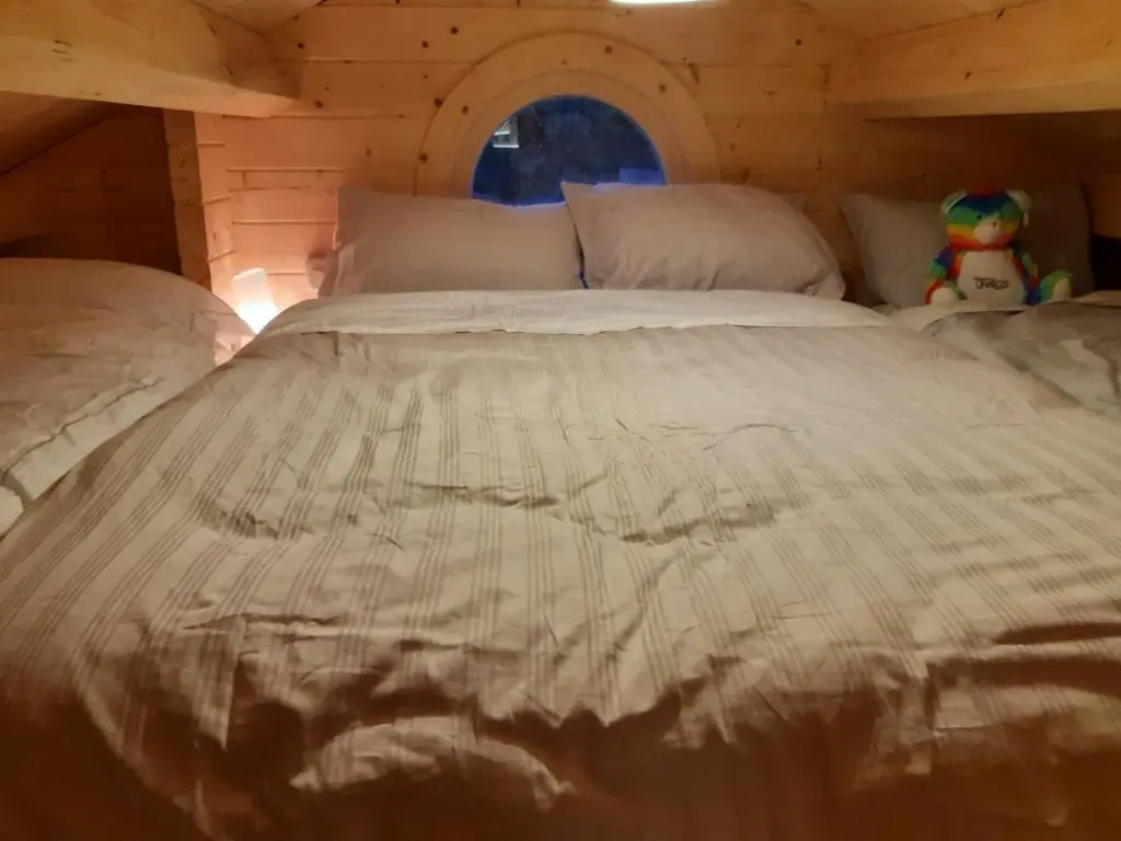 a bed in a wooden cabin with a white comforter at Springbank Cabin in Insch