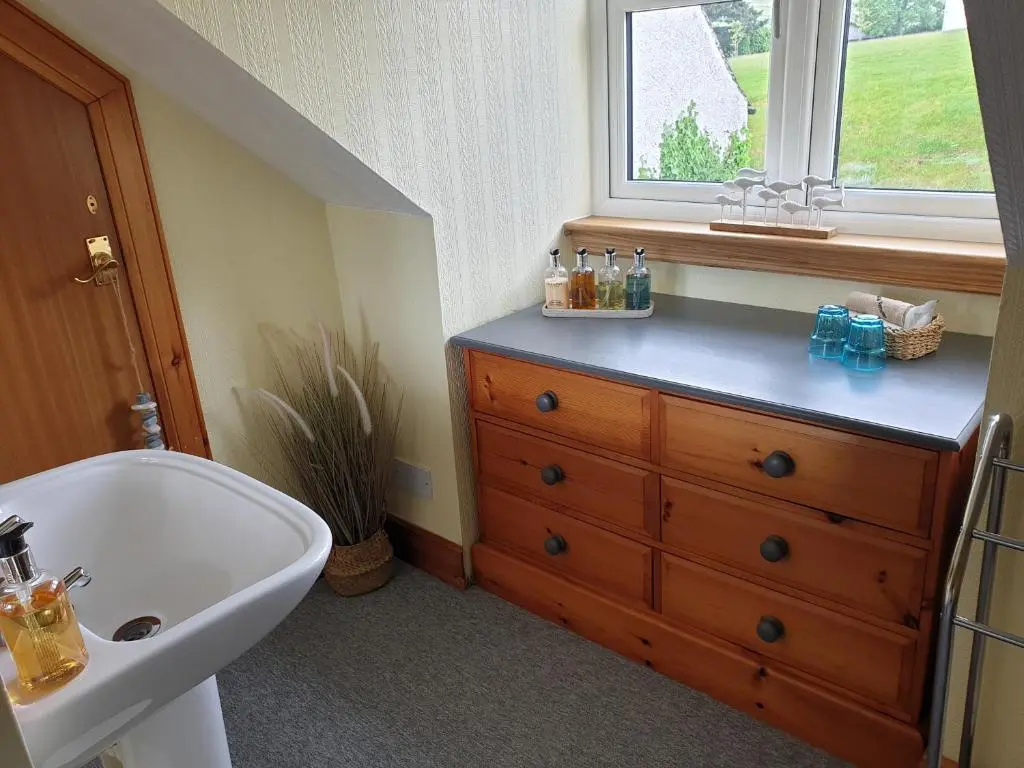 a bathroom with a sink and a wooden dresser at Lorien House B&B in Fort Augustus