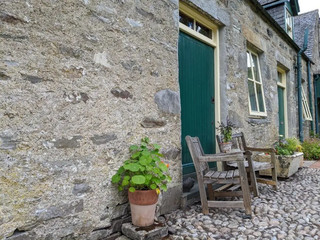 a stone building with a green door and a chair at Stable Cottage, CrannachCottages in Garve