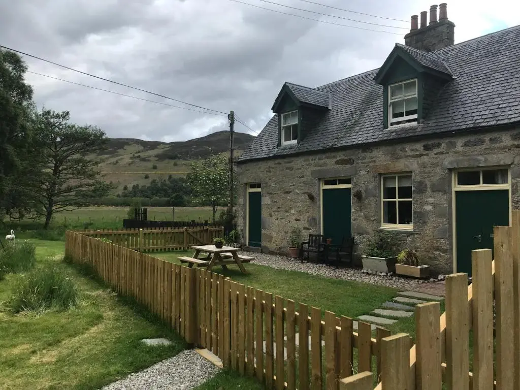 a house with a wooden fence and a picnic table at Stable Cottage, CrannachCottages in Garve