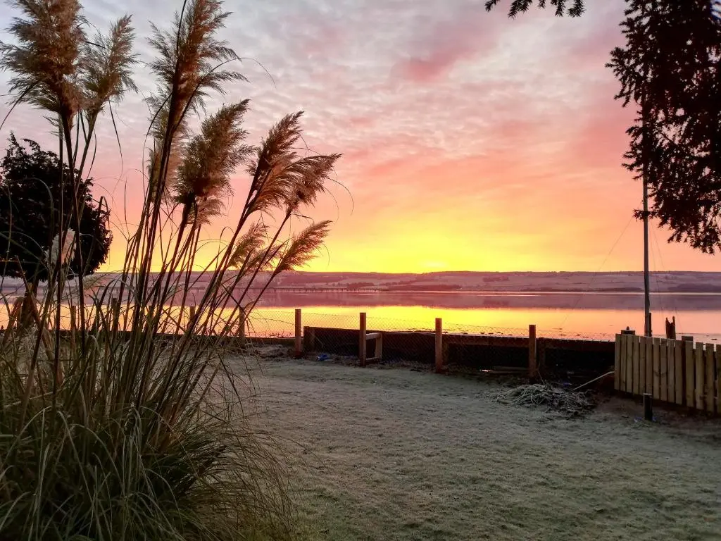 a sunset on the beach with a fence and palm trees at St Brighs in Dingwall