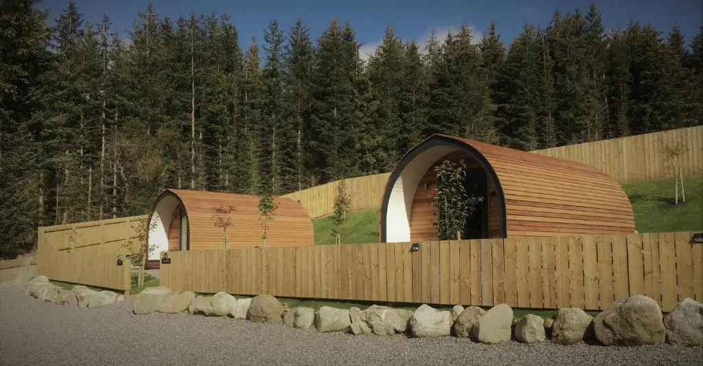 two wooden buildings with a fence and some trees at Tomatin Glamping Pods in Inverness