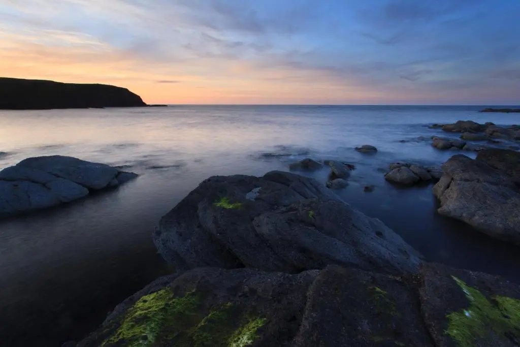 a beach with rocks in the water at sunset at Mill Of Nethermill Holidays in Pennan