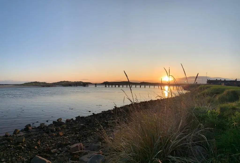 a sunset over a body of water with a pier at Hayfield Apartment in Lossiemouth