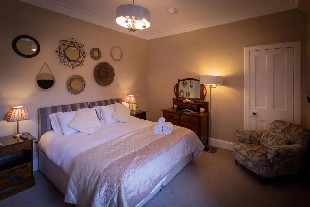 a bedroom with a large bed and a chair at Craigellachie Lodge in Craigellachie