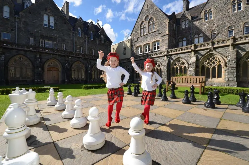 two children playing a game of chess in front of a building at Loch Ness Moat House Apartments in Fort Augustus