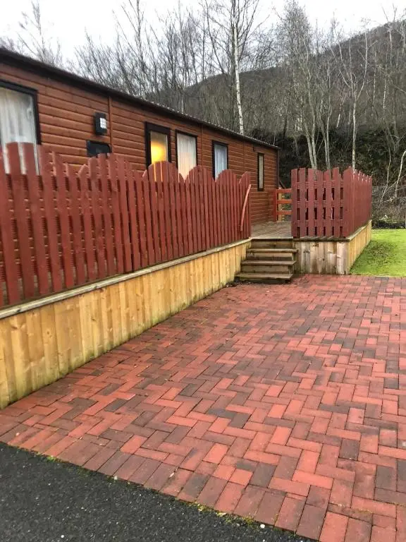 a house with a red fence and a brick driveway at 81 The Heathers, Aviemore Holiday Park , Dalfaber rd Aviemore PH22 1PX in Aviemore