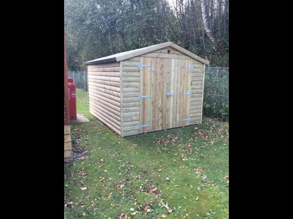 a wooden shed sitting in the grass next to a fire hydrant at 81 The Heathers, Aviemore Holiday Park , Dalfaber rd Aviemore PH22 1PX in Aviemore