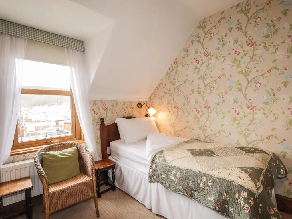 a bedroom with a bed and a chair and a window at Glencanisp in Aviemore