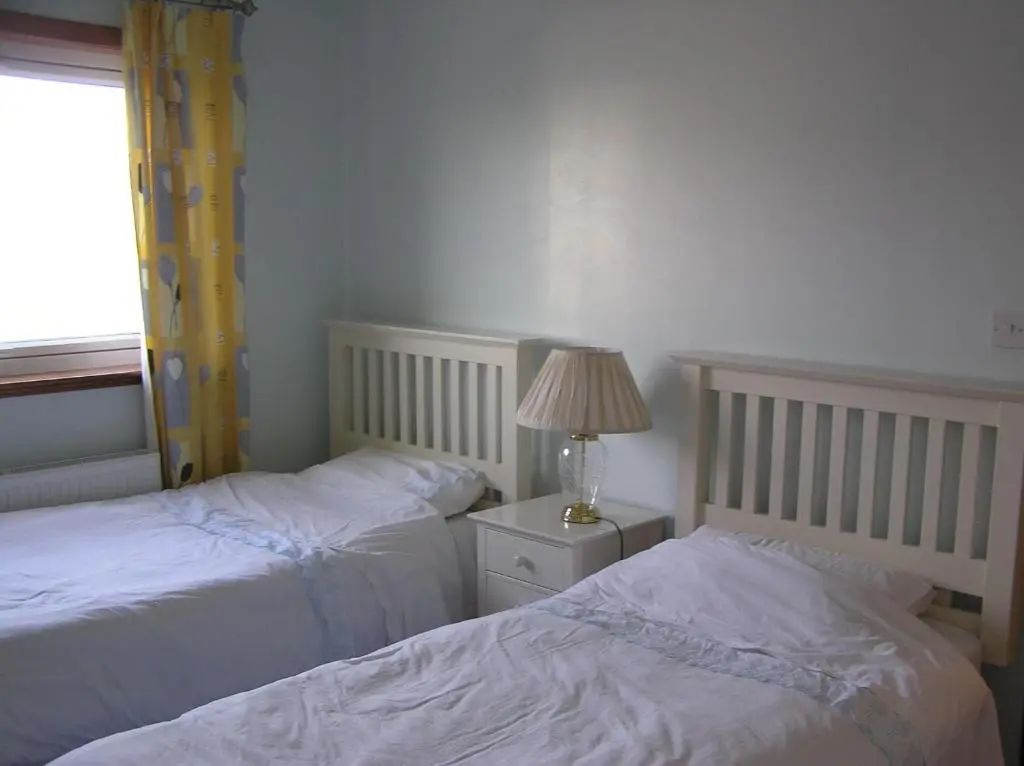 a bedroom with two beds and a lamp and a window at The Antlers in Lybster