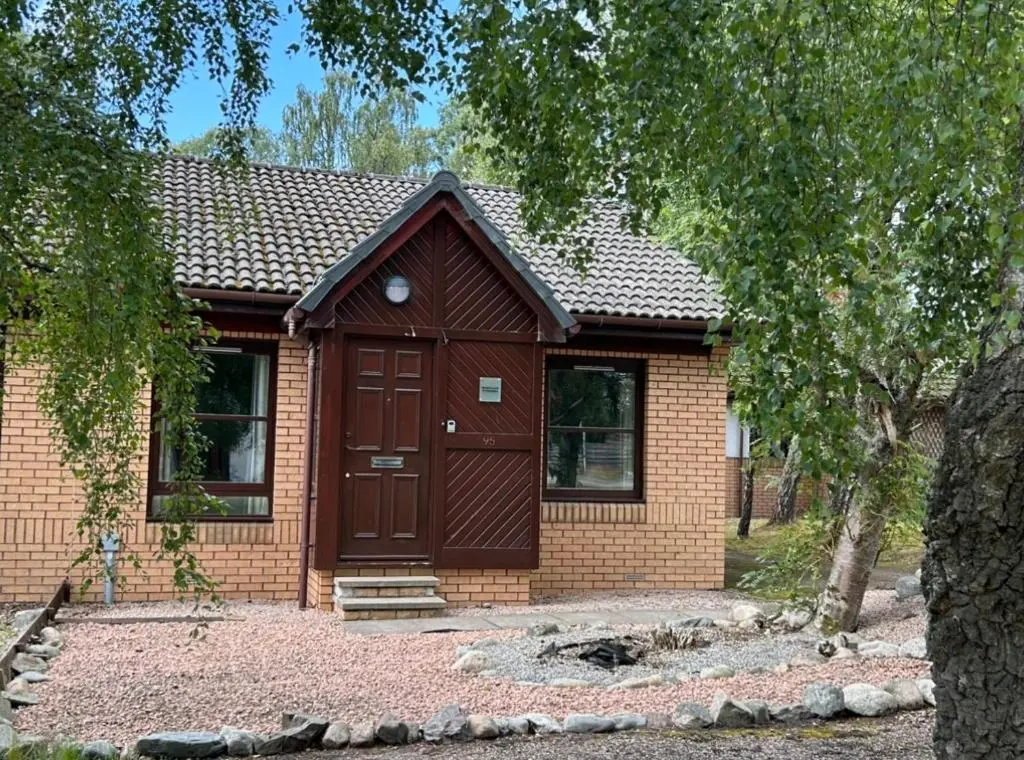 a house with a brown door and a tree at Rendezvous , Aviemore in Aviemore