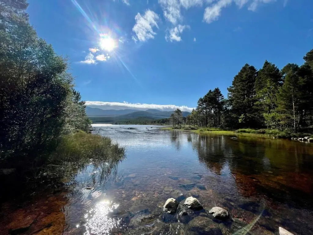 a river with rocks and the sun in the sky at Golden Eagle Lodge in Kingussie