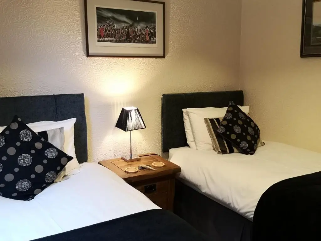 a room with two beds and a lamp on a table at Cranford Guest House in Braemar