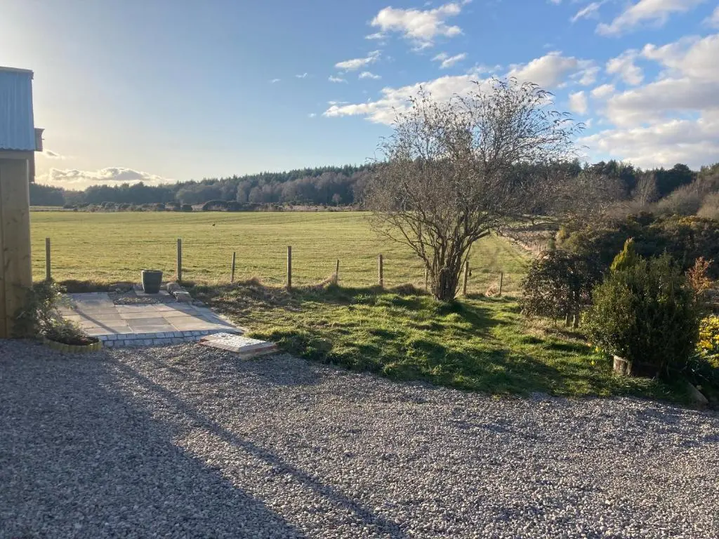 a field with a fence and a tree next to a building at Clashmore Wood in Dornoch
