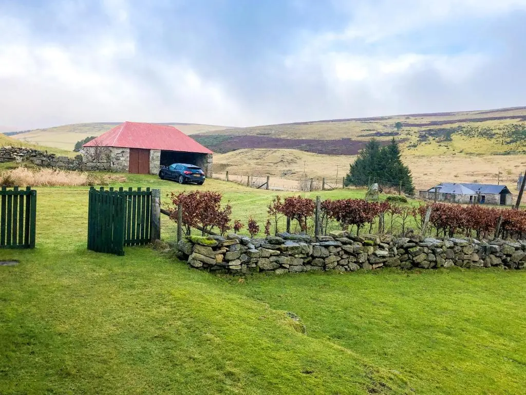 a car parked in a field with a stone wall at Crofts in Badenyon