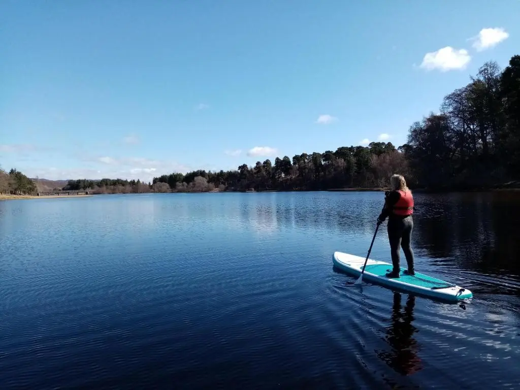 a woman standing on a paddle board on a lake at Brooklynn Guest House in Grantown on Spey