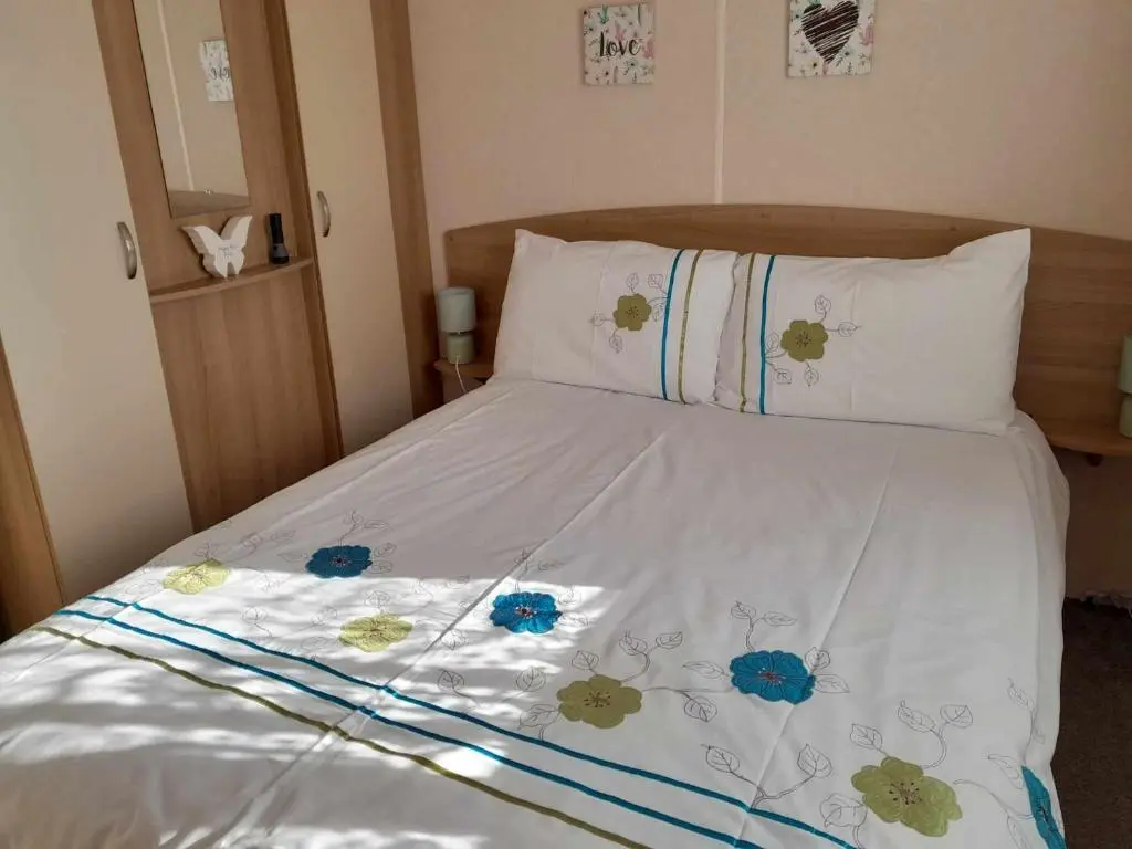 a bed with a white comforter with flowers on it at hollies retreat in Lossiemouth