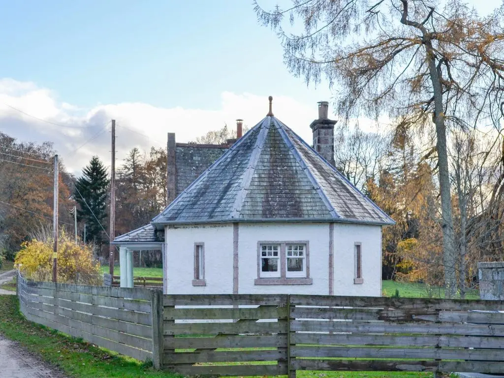 a small white house behind a wooden fence at Dairy Cottage in Whitehouse