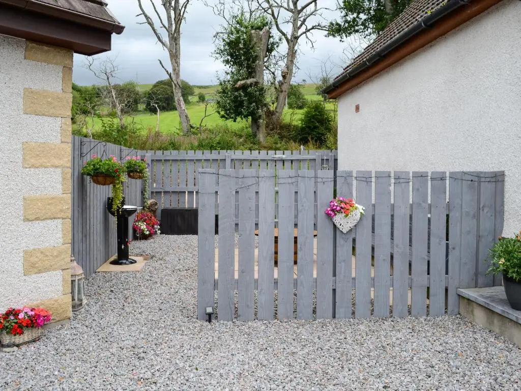 a fence with flowers on it next to a house at Rose Cottage in Dingwall
