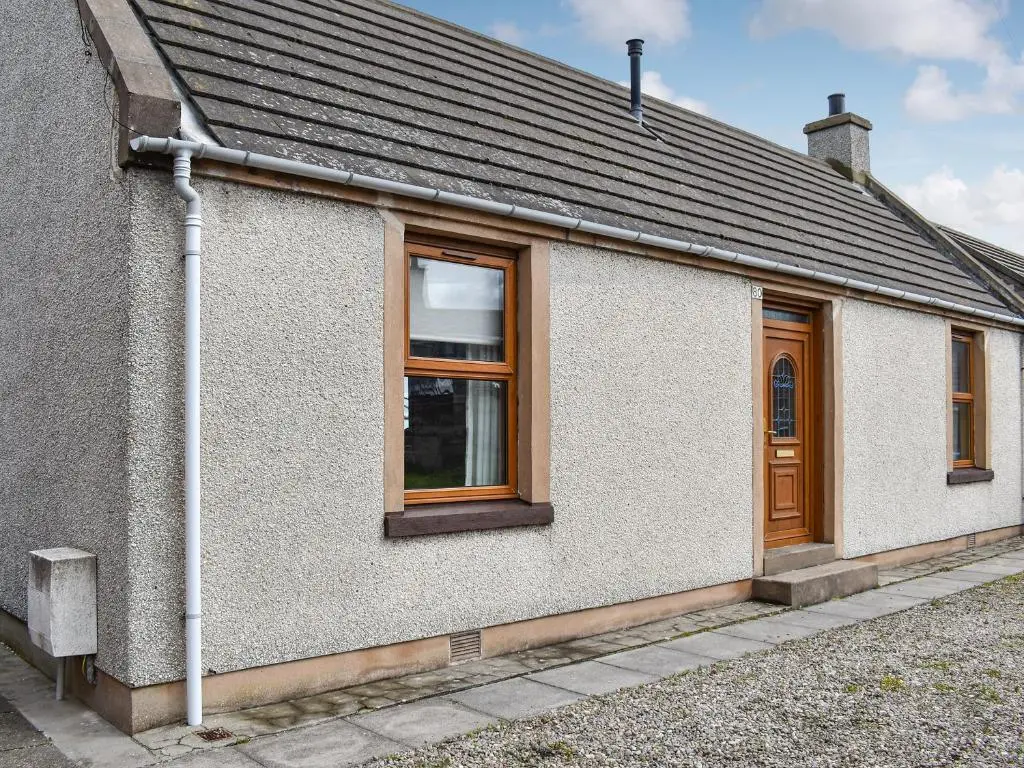 a white house with wooden doors and windows at Sea Breeze Cottage in Buckie