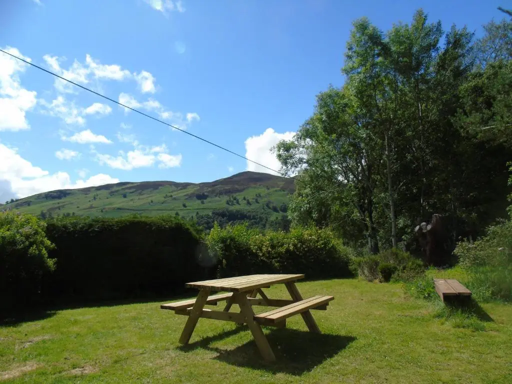 a picnic table in the grass with a hill in the background at Thistle Cottage, CrannachCottages in Garve
